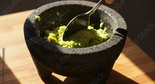 Process shot of spoon mashing fresh avocado in a molcajete under warm, natural light.