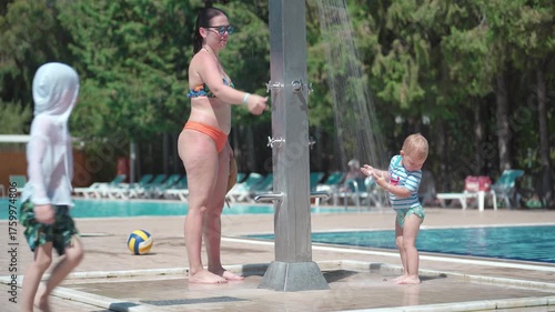Two young children and their mother are washing in the shower next to the swimming pool.