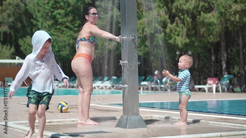 Two young children and their mother are washing in the shower next to the swimming pool.