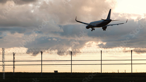 Passenger plane landing at airport behind barbed wire fence at sunset