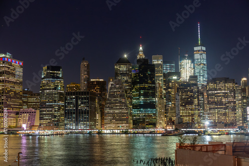 Nighttime view of Manhattan's skyline from the Brooklyn Promenade, showcasing illuminated skyscrapers along the East River of the NYC Skyline in the Financial District