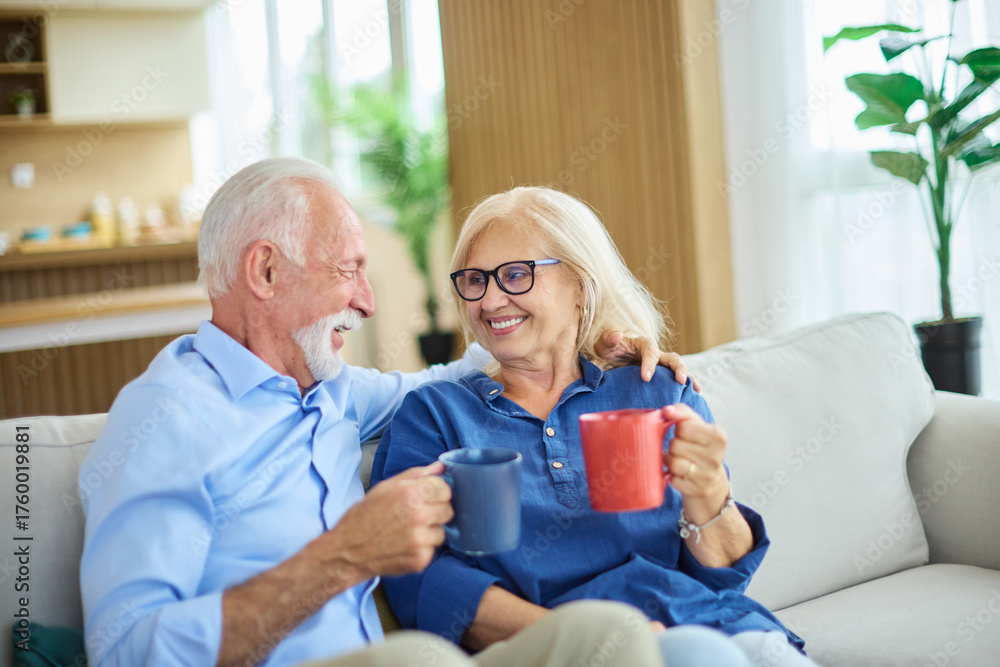 Obraz premium Portrait of a happy senior couple embracing talking and drinking coffee or tea at home