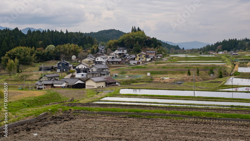 Scenic view of rural Japan with traditional houses and terraced rice fields under a cloudy sky
