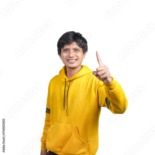 Young man in a yellow hoodie smiling while pointing upward with one finger, isolated on transparent background. Concept of idea, number one, or attention.