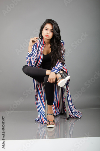 A female dancer sits on a metal stool, striking a lively, expressive pose as her striped long coat swirls around her. Perfect for fashion, lifestyle, empowerment, and creative movement concepts.