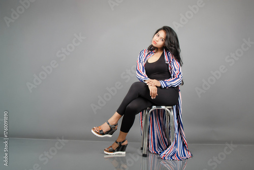 A female dancer sits on a metal stool, striking a lively, expressive pose as her striped long coat swirls around her. Perfect for fashion, lifestyle, empowerment, and creative movement concepts.
