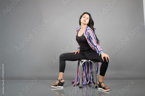 A female dancer sits on a metal stool, striking a lively, expressive pose as her striped long coat swirls around her. Perfect for fashion, lifestyle, empowerment, and creative movement concepts.