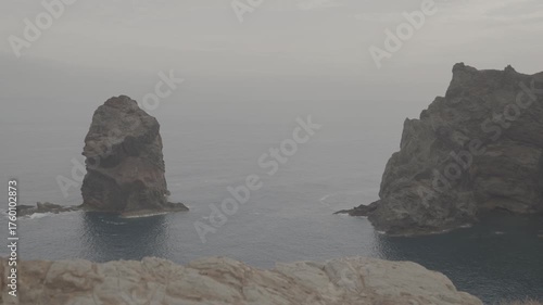 Wide shot of tall sea stacks and volcanic cliff in Madeira Portugal against calm ocean backdrop (SLOG3)