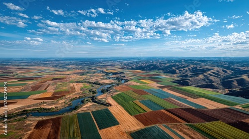 Aerial view of expansive colorful patchwork farmland with cultivated fields, vibrant crop patterns, distant rolling hills, blue sky with scattered clouds, scenic rural landscape