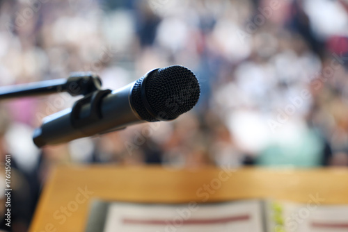 Фотография A single black microphone isolated against a blurred lecturn and background of people or audience
