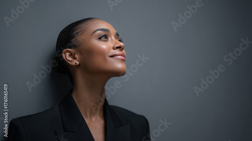 Confident black woman looking forward with slight smile wearing black blazer against solid gray background