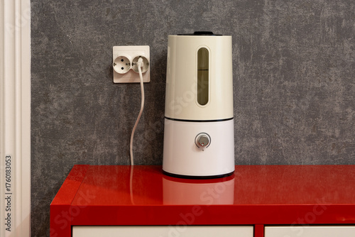 Air humidifier. An electric air humidifier stands on a red chest of drawers near a gray wall in a living room in an apartment. Close-up. Household appliances.