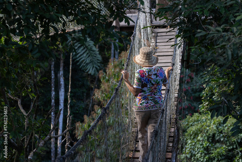 Canopy Explorer: a vibrant and engaging photograph of a solitary explorer traversing a narrow suspension bridge high in the Peru's Amazon rainforest canopy