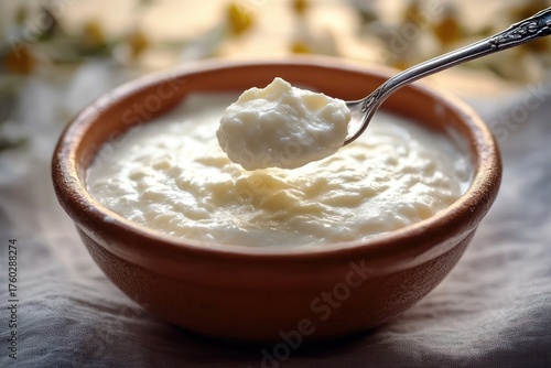 Close-up of creamy white yogurt or curd served in a brown ceramic bowl with a silver spoon lifting a spoonful, soft natural light creating a cozy atmosphere