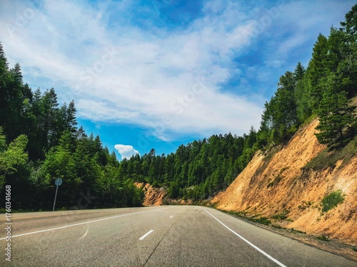 A view from a car on a small country road, surrounded by forests and mountain cliffs on either side. Cinematic.