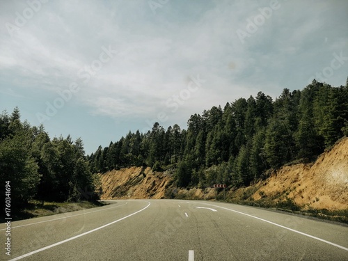 A view from a car on a small country road, surrounded by forests and mountain cliffs on either side. Cinematic depth effect.
