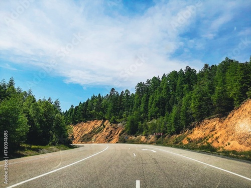 A view from a car on a country road, surrounded by forests and mountain cliffs on either side. Cinematic blue effect.