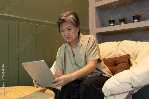 An elderly asian woman using her tablet in a cozy living room, enjoying digital communication