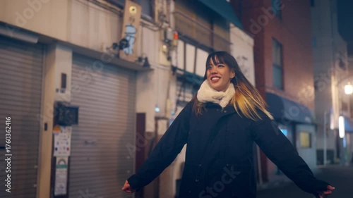 Happy Young Asian woman walking city street in winter night. Attractive girl enjoy outdoor lifestyle travel Tokyo city, Japan and looking illuminated neon lights at night.