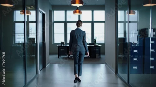 Confident businesswoman in suit walking down modern office hallway with back view