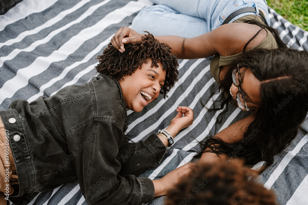 Obraz premium A woman puts her hand on the head of her female friend while they laugh and lie on a blanket