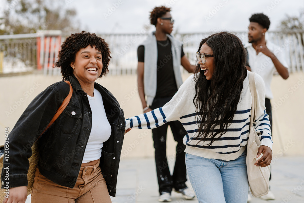 Obraz premium Two female friends are laughing and holding hands as they walk in front of two male friends who are talking