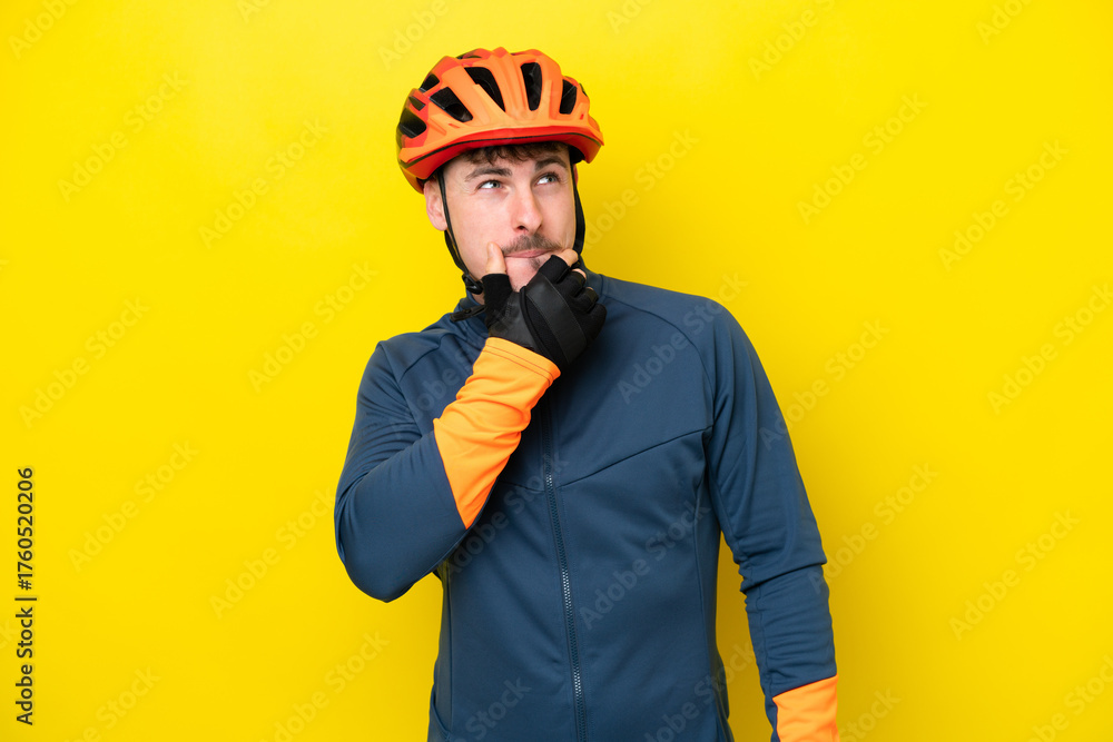Fototapeta premium Young cyclist caucasian man isolated on yellow background having doubts and thinking