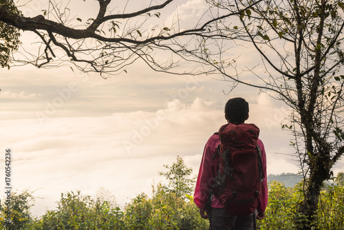 Traveler with backpack standing on mountain top looking at scenic sunrise over sea of mist, adventure lifestyle concept, hiking, freedom, exploration and outdoor travel inspiration.