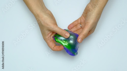 Human hands squeeze a viscous colorful slime. View from above. On a white background. Relaxation, calming down. 