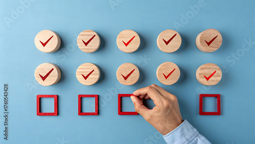 Hand completing a checklist with wooden circles and red check marks, placing a red square to signify completion on a blue textured background