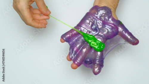 Human hands squeeze a viscous colorful slime. View from above. On a white background. Relaxation, calming down. 