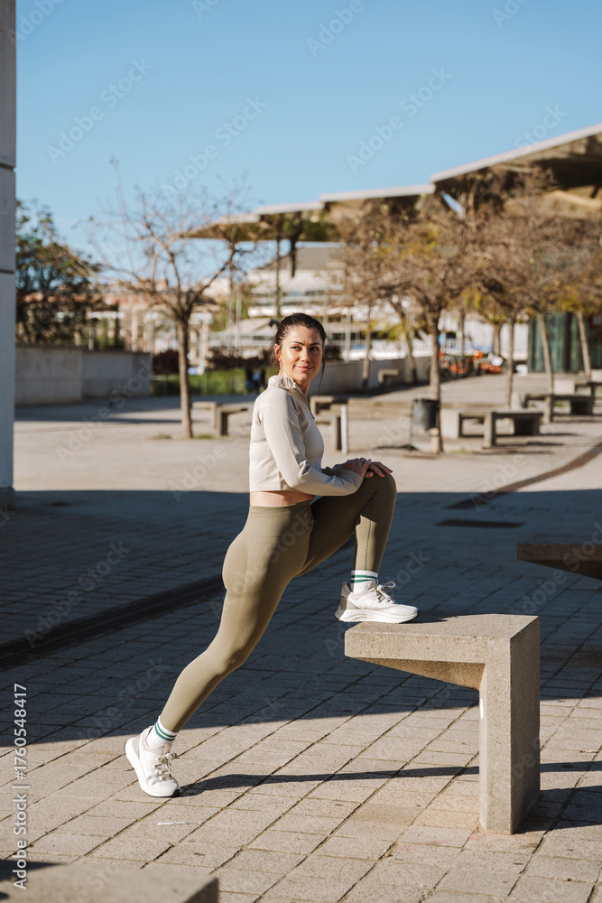 Fototapeta premium A woman warms up and stretches while resting her foot on a stone stool