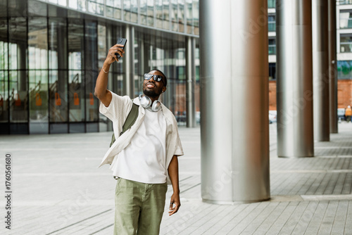 Fotografija Male worker smiling and holding up his phone while standing and posing