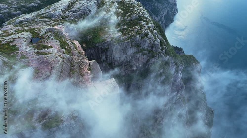 Immerse yourself in the breathtaking views from Preikestolen in Norway. Discover the dramatic cliffs and serene fjord surrounded by fluffy clouds and vibrant greenery.