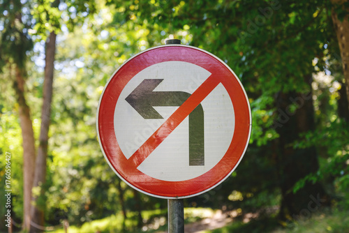 No left turn traffic sign placed outdoors with green leafy trees in the background on a sunny day.