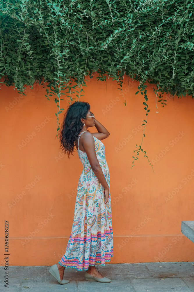 Obraz premium A woman in a long dress stands in front of a wall with green vines growing on it