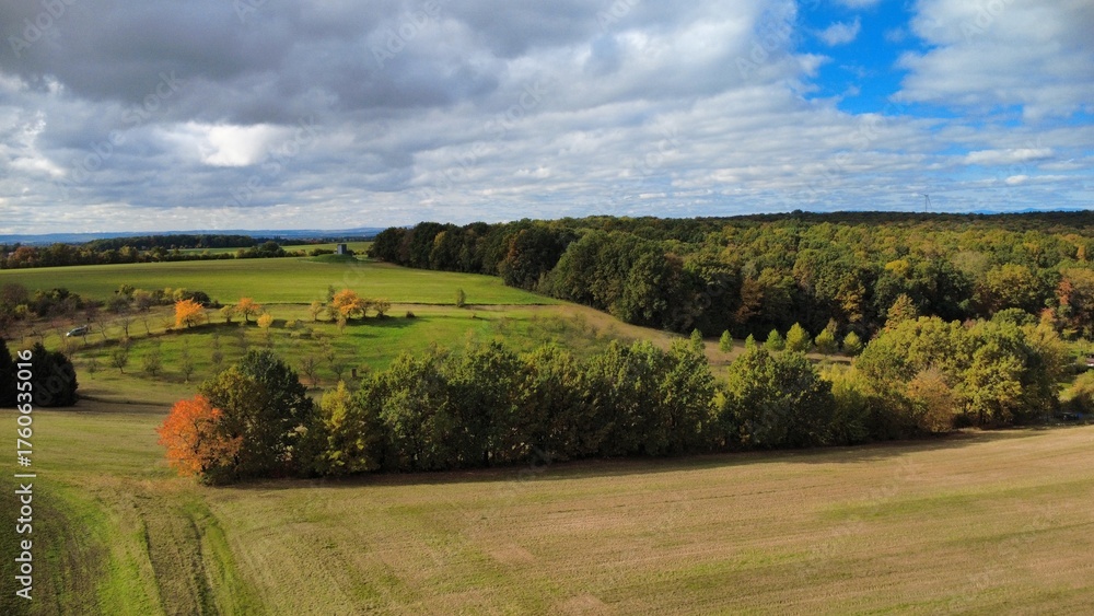 Fototapeta premium Beautiful sunny day with green fields and colorful trees on the horizon of the Czech countryside. Aerial drone view capturing the vibrant autumn landscape 