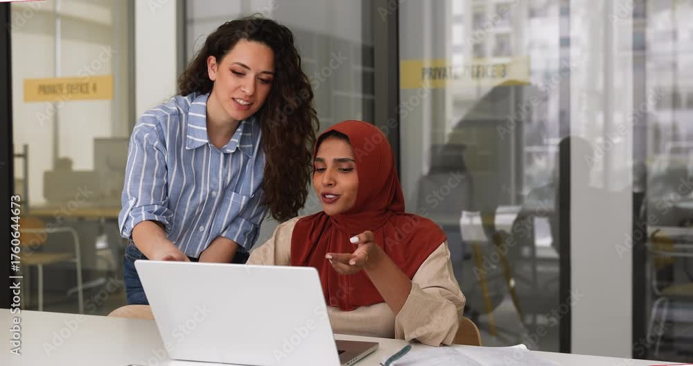 Positive diverse young female managers working at laptop together