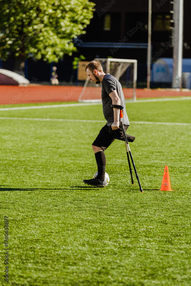 Obraz premium A man on crutches runs and dribbles a ball after a cone