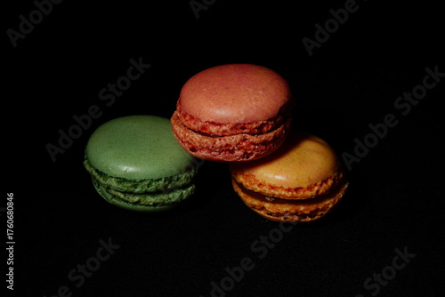 Assortment of colorful macarons arranged on a dark background. French almond cookies with different flavors and vibrant colors, displayed in a minimalist food composition