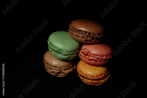 Assortment of colorful macarons arranged on a dark background. French almond cookies with different flavors and vibrant colors, displayed in a minimalist food composition