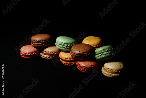 Assortment of colorful macarons arranged on a dark background. French almond cookies with different flavors and vibrant colors, displayed in a minimalist food composition