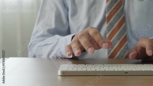 businessman typing on white wireless keyboard in office with close up of male hands in formal shirt and striped tie at desk in natural daylight focused and professional atmosphere