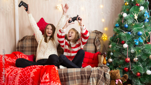 Happy family mother and daughter laugh and play video games together using a video game console on christmas holiday