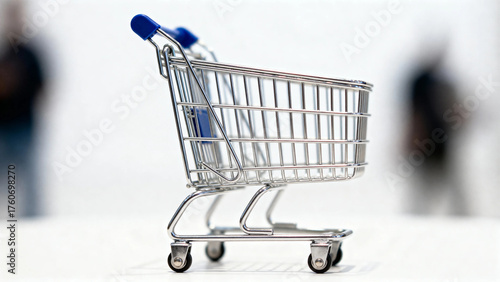 A small metal shopping cart with blue handles on a white surface, with blurred figures in the background.