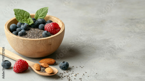 Healthy bowl of chia seeds topped with fresh blueberries, raspberries, and almonds, garnished with mint leaves, perfect for nutritious snack or breakfast option
