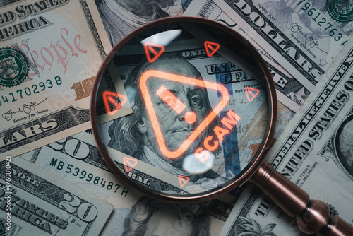 Magnifying glass focusing on scam warning symbol over dollar bills concept of financial fraud money laundering cybercrime and online scam alert for security awareness and finance protection