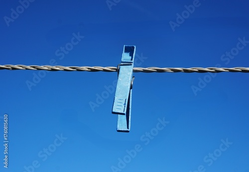 Zbliżenie na niebieską klamerkę przypiętą do sznurka. Wyraźna faktura plastiku i kształt spinacza.