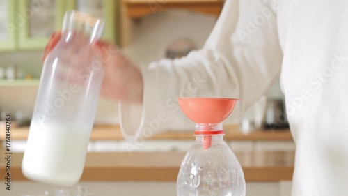 Person is pouring milk into a bottle. The bottle is orange and has a red top