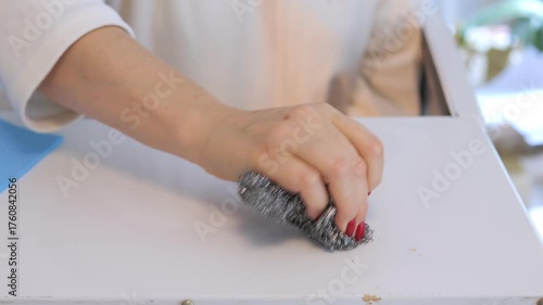 Woman is polishing a white surface with a metal scrubber. The surface is white and the woman is using a blue cloth